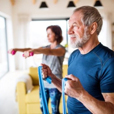 Older man and woman exercising at home with elastics and weights.
